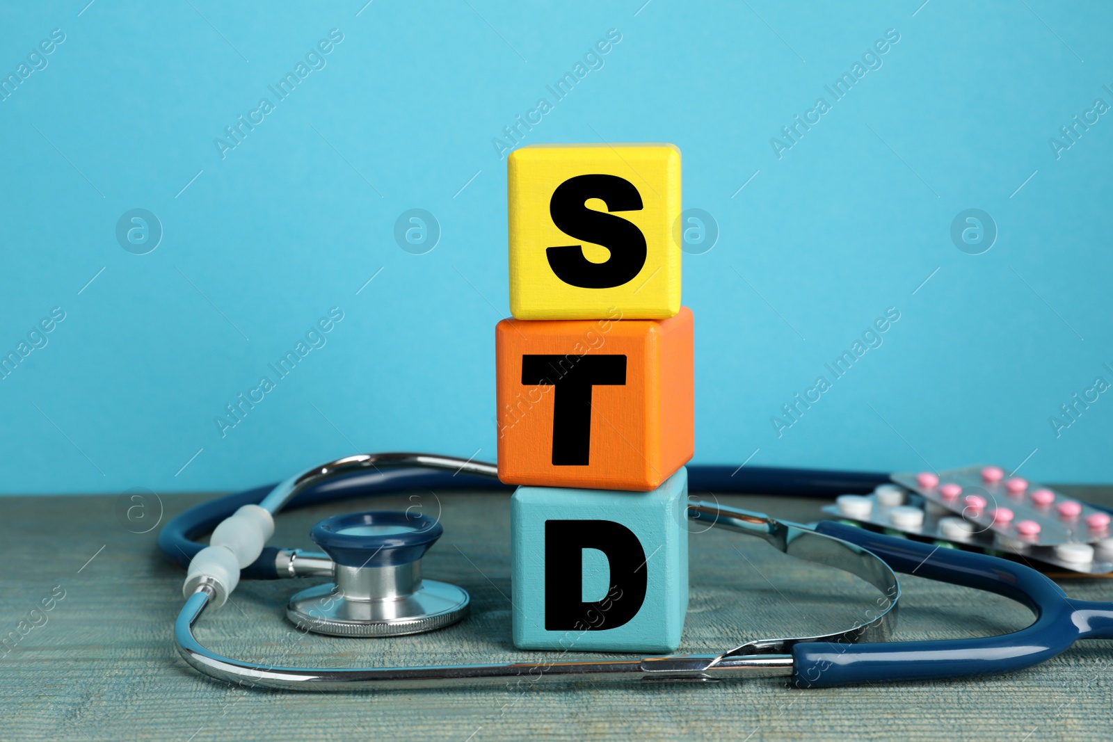 Photo of Abbreviation STD made with cubes near stethoscope and pills on light blue wooden table