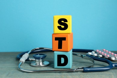 Abbreviation STD made with cubes near stethoscope and pills on light blue wooden table