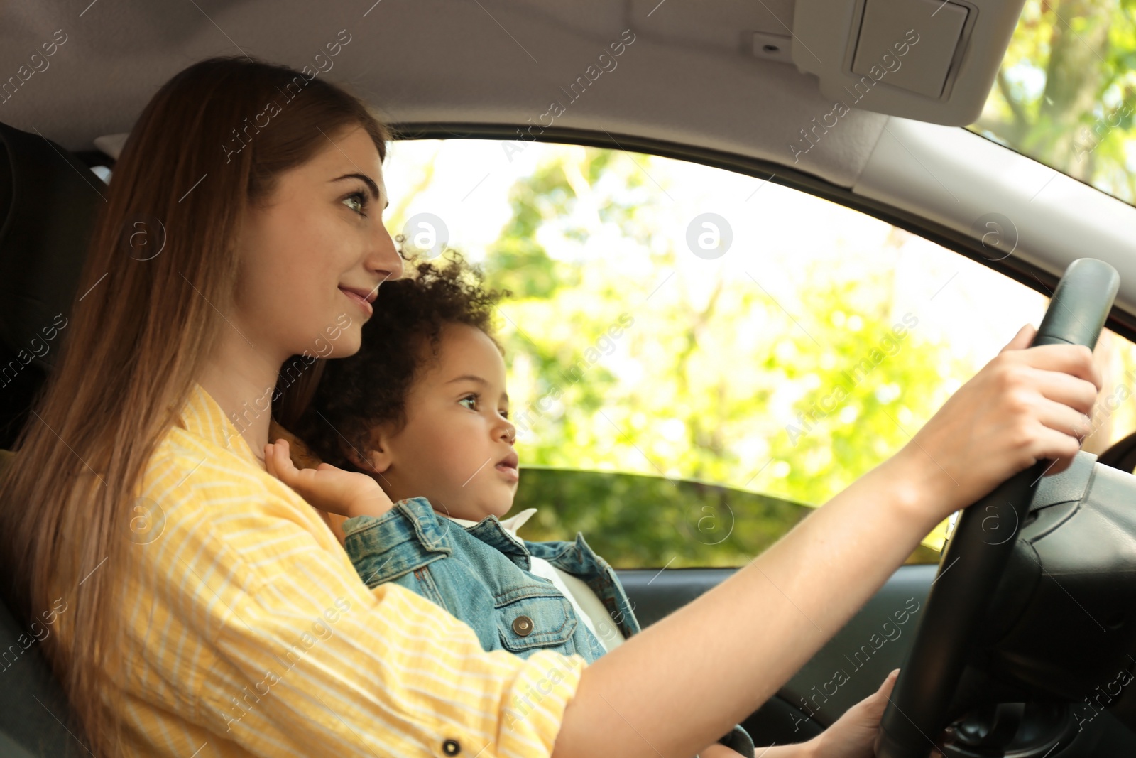 Photo of Mother with cute little daughter driving car together. Child in danger