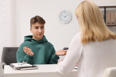 Psychologist working with teenage boy at table in office