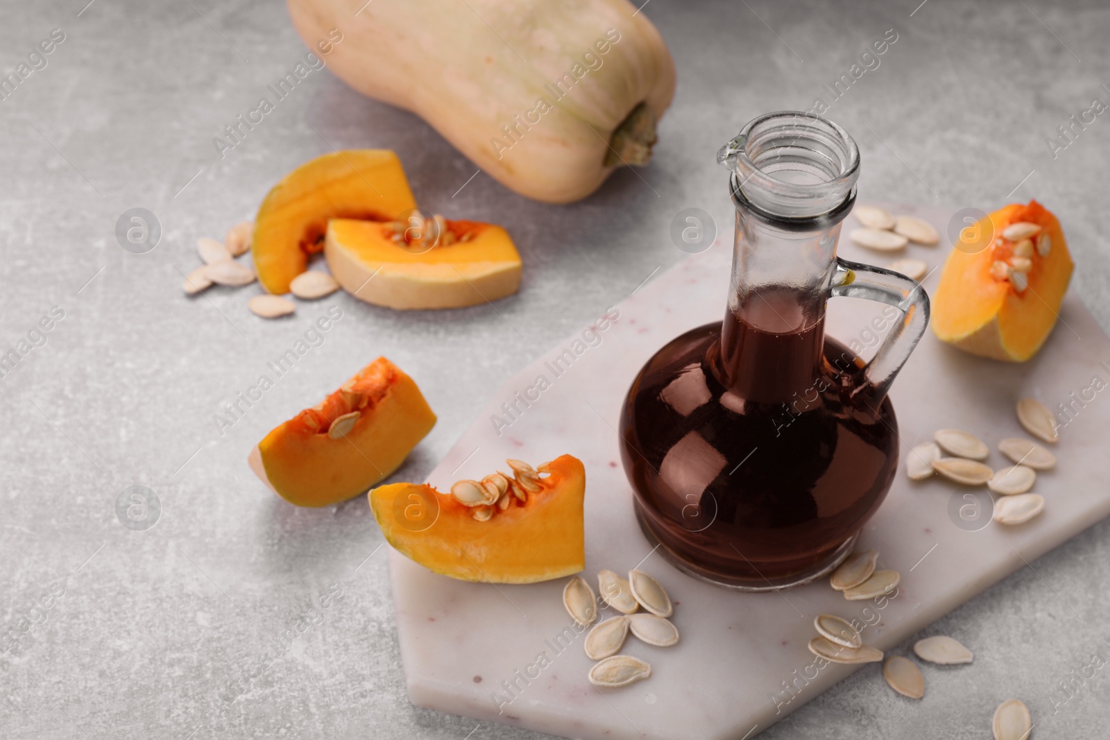 Photo of Fresh pumpkin seed oil in glass jug on grey table. Space for text