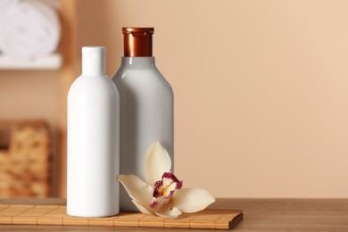 Photo of Bottlesshampoo and flower on wooden table in bathroom, space for text