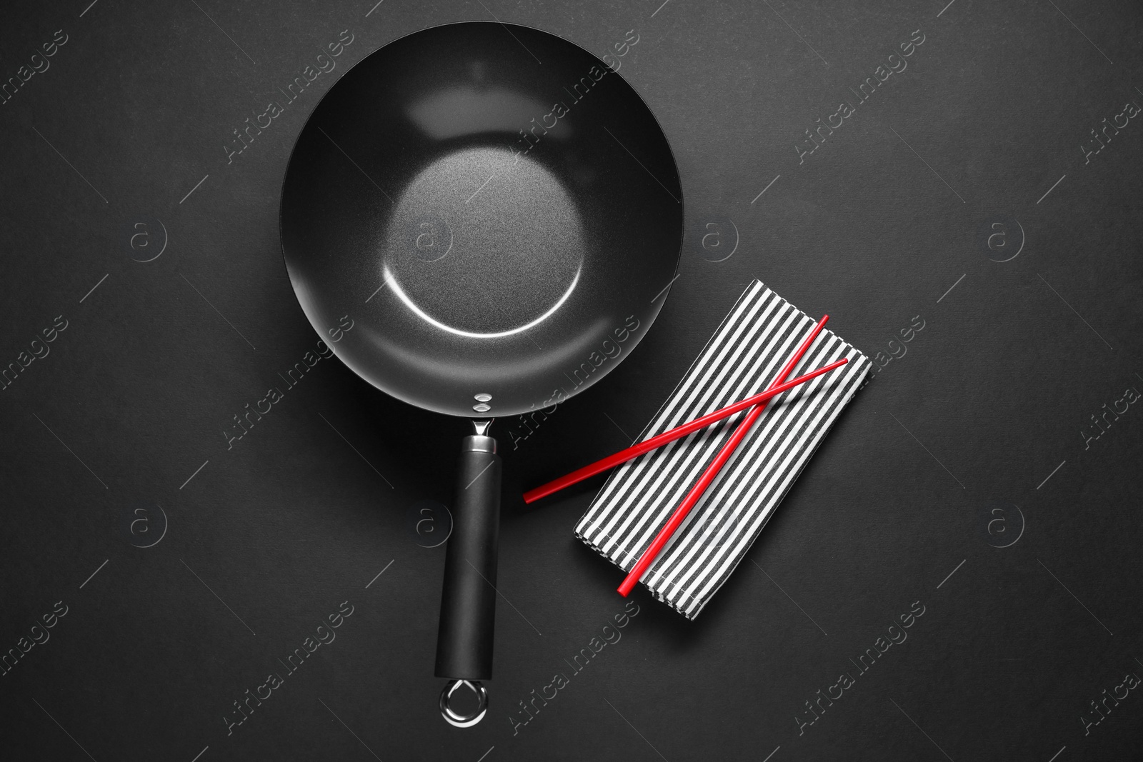 Photo of Empty iron wok and chopsticks on black table, flat lay