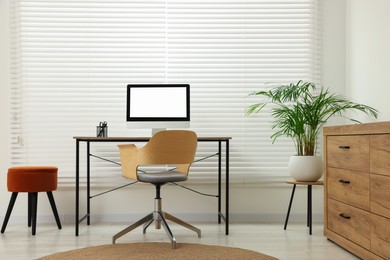 Photo of Stylish office interior with comfortable chair, desk, computer and houseplant