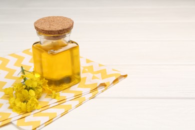 Rapeseed oil in glass bottle and beautiful yellow flowers on white wooden table, space for text