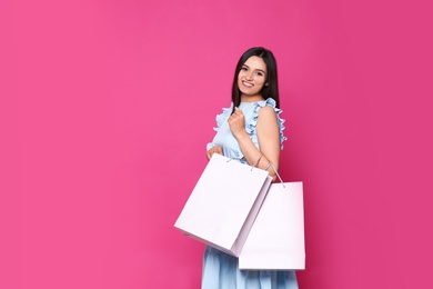 Beautiful young woman with blank paper bags against color background, space for text