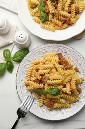 Delicious pasta with minced meat and basil served on white marble table, flat lay
