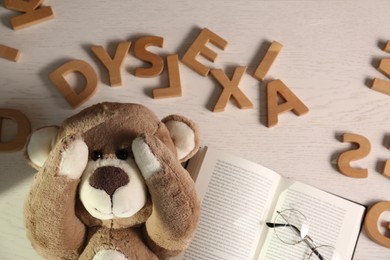 Word Dyslexia made of letters, teddy bear and book on light wooden table, flat lay