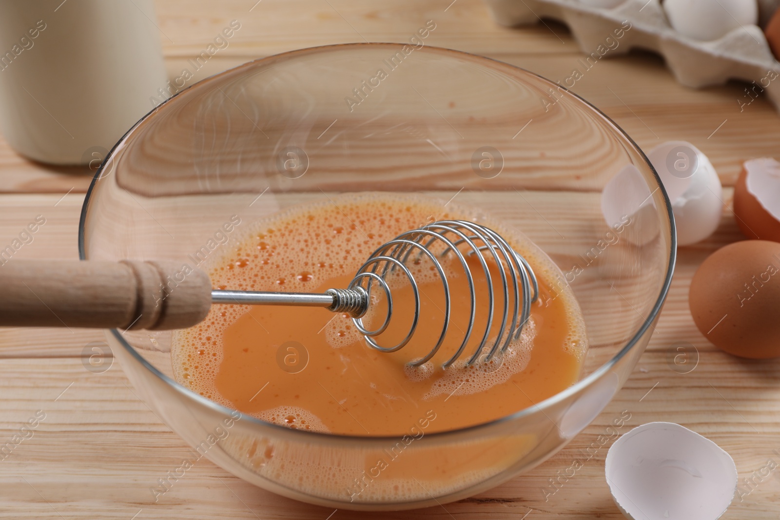 Photo of Making dough. Beaten eggs in bowl and shells on wooden table, closeup