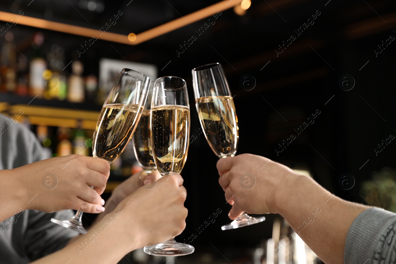 Photo of Friends clinking with glasses of champagne in bar, closeup