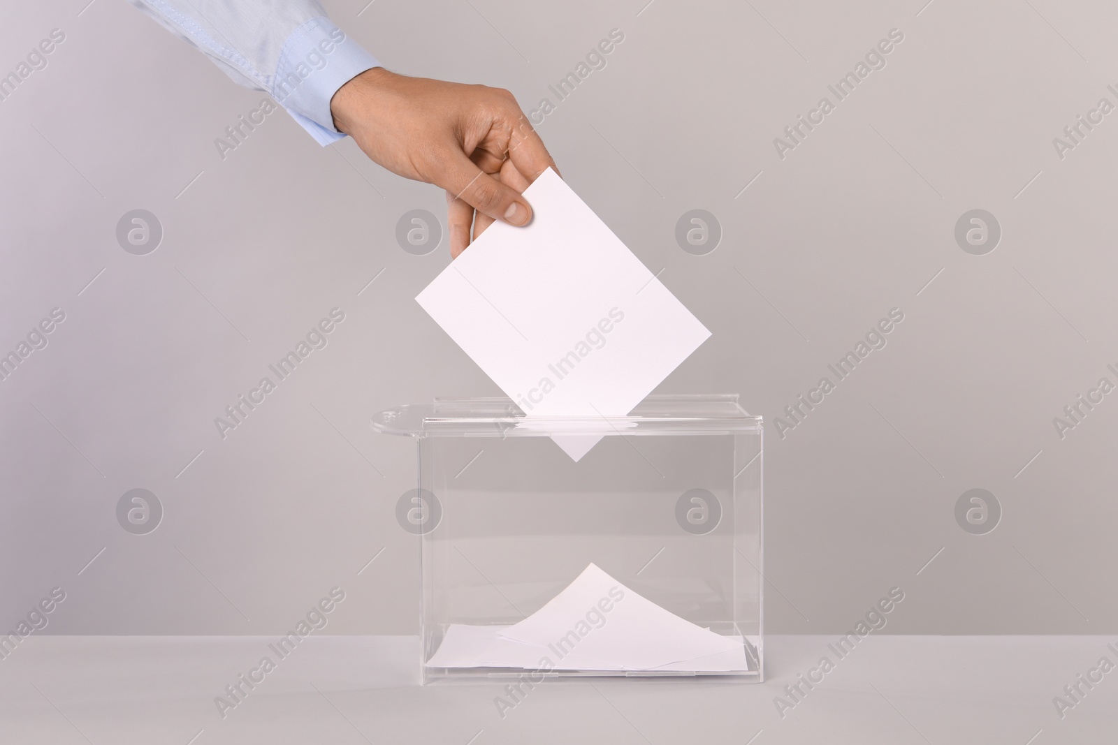 Photo of Man putting his vote into ballot box on light grey background, closeup