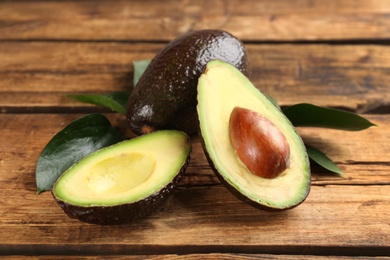 Photo of Whole and cut avocados with green leaves on wooden table, closeup