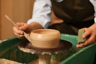 Photo of Clay crafting. Woman making bowl with modeling tool on potter's wheel, closeup