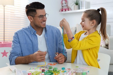Photo of Happy father with his cute daughter making beaded jewelry at table in room
