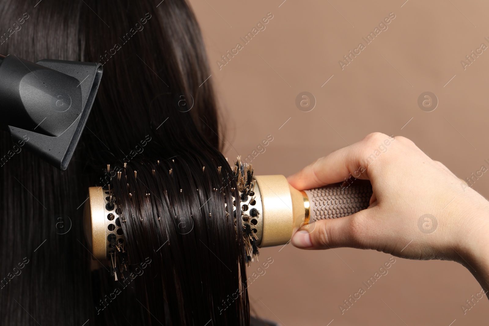 Photo of Hairdresser blow drying client's hair on light brown background, closeup