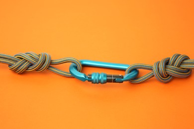 Photo of One metal carabiner with ropes on orange background, space for text
