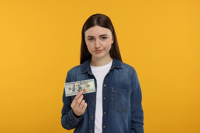 Sad woman with dollar banknote on orange background