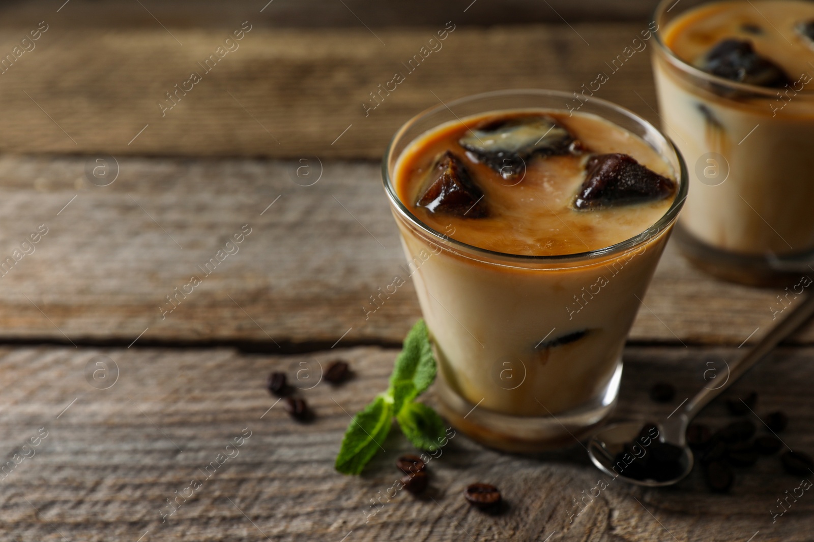 Photo of Glasses of delicious iced coffee with milk, beans and mint on wooden table, closeup. Space for text
