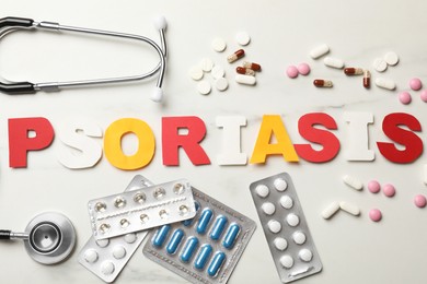 Word Psoriasis made of paper letters, stethoscope and pills on white table, flat lay