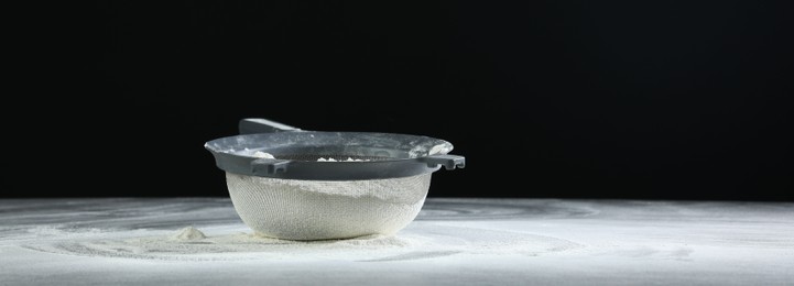 Photo of Sieve with flour on table against black background, space for text