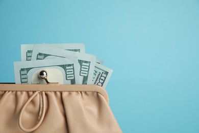 Photo of One stylish leather purse with money on light blue background, closeup. Space for text