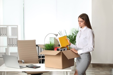 Photo of Upset young woman packing stuff in box at office