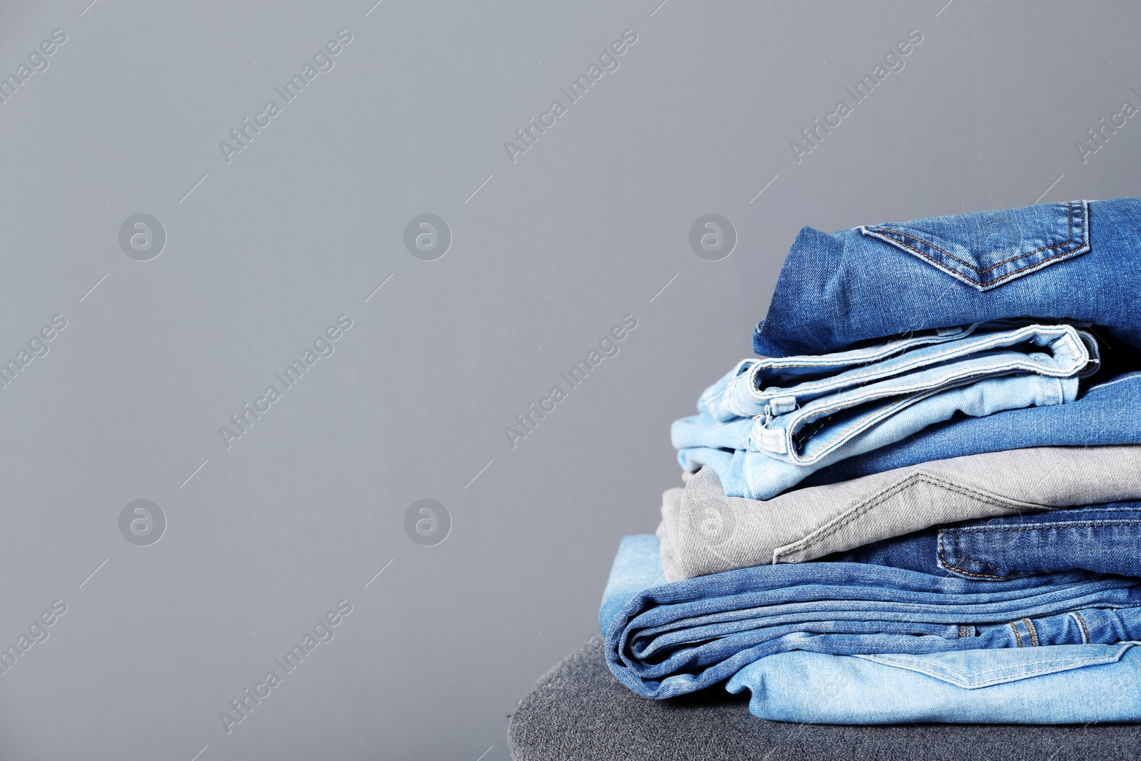 Photo of Stack of different jeans on stool against gray background. Space for text