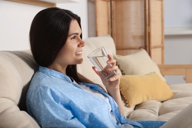 Photo of Happy young woman drinking water indoors. Refreshing drink