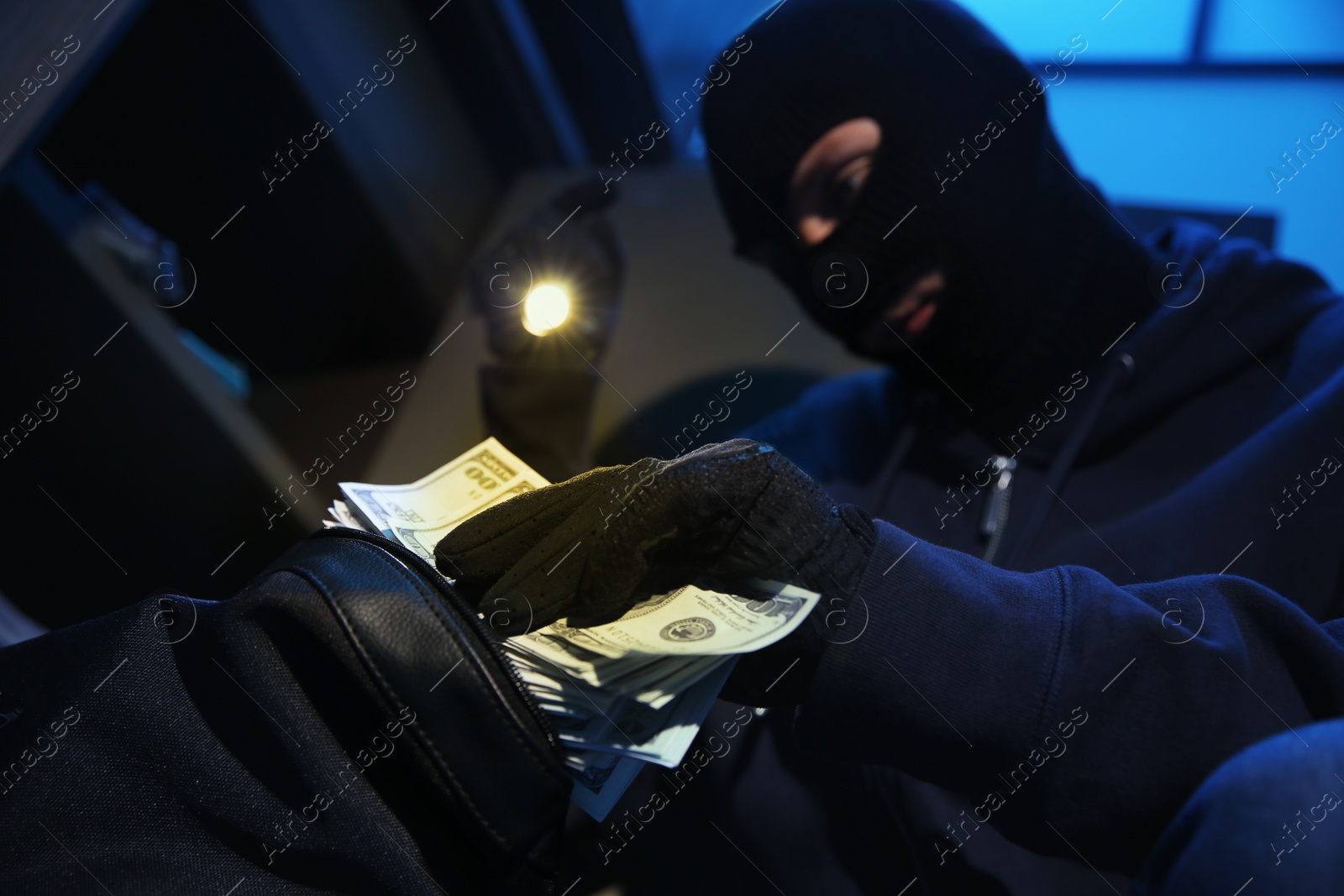 Photo of Thief taking money out of steel safe indoors at night, closeup