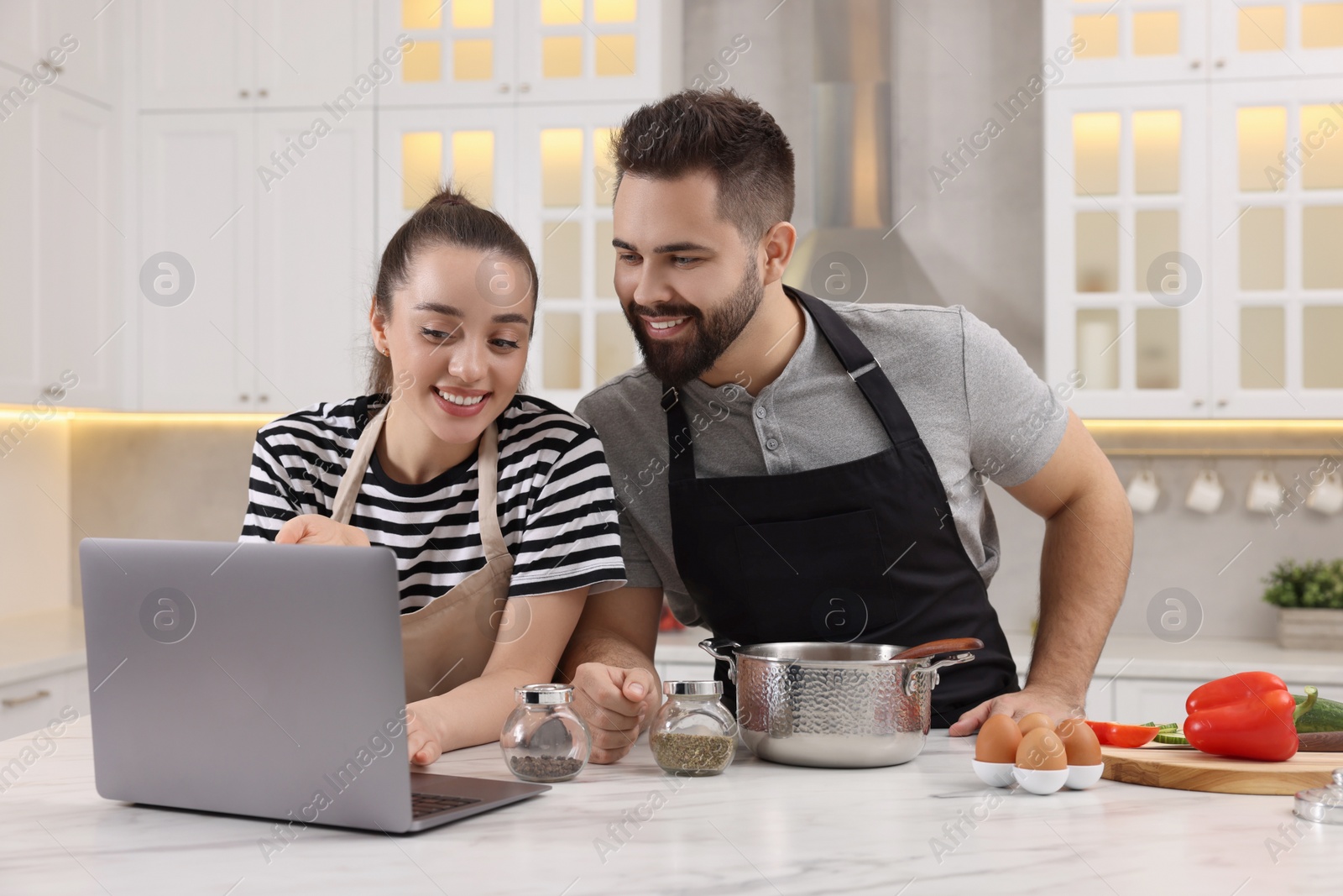 Photo of Happy lovely couple using laptop while cooking in kitchen