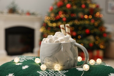 Photo of Christmas cocoa with marshmallows and wafer sticks in cup on green sweater indoors, closeup