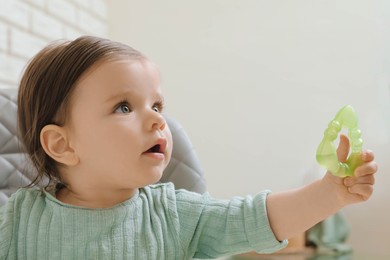 Cute little baby with teether in high chair indoors