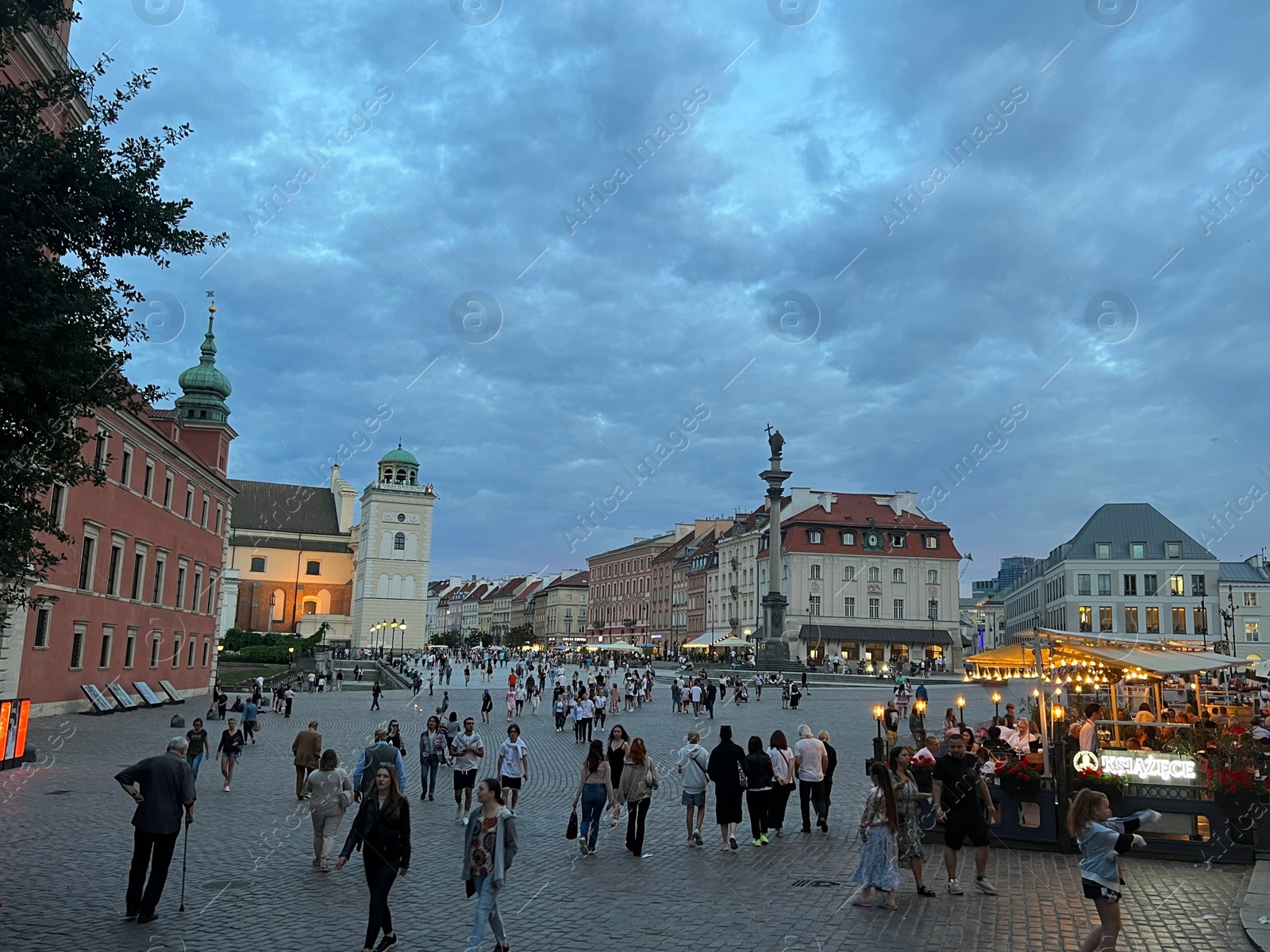 Photo of WARSAW, POLAND - JULY 15, 2022: View of crowded Old Town Market Place under cloudy sky in evening