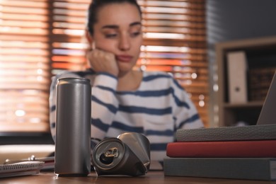 Photo of Tired young woman with energy drink studying at home, focus on cans