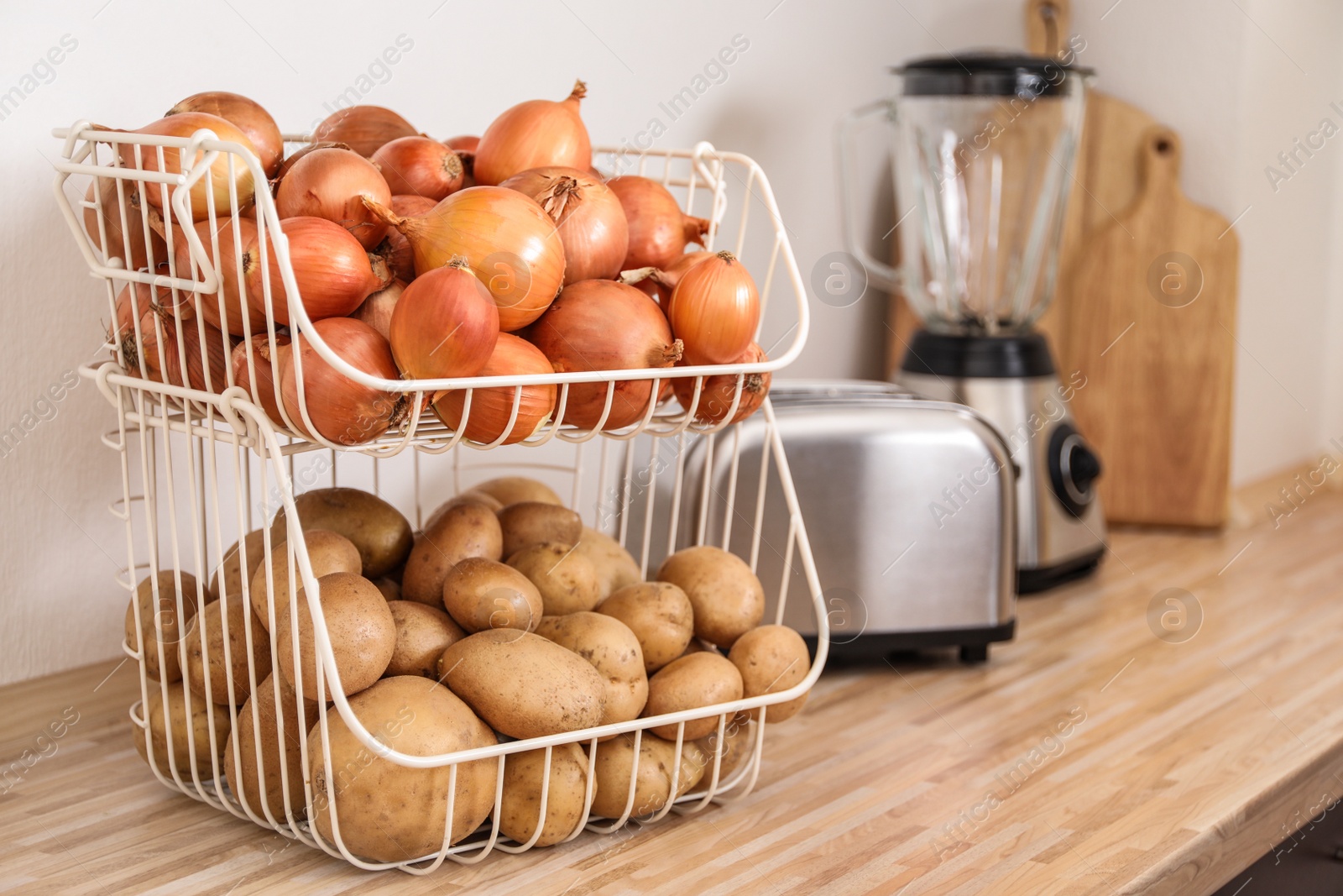 Photo of Container with potatoes and onions on wooden kitchen counter, space for text. Orderly storage