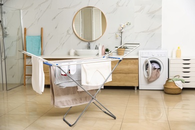 Photo of Clean laundry hanging on drying rack in bathroom