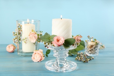 Photo of Glass candlestick, holders, burning candles and floral decor on light blue wooden table