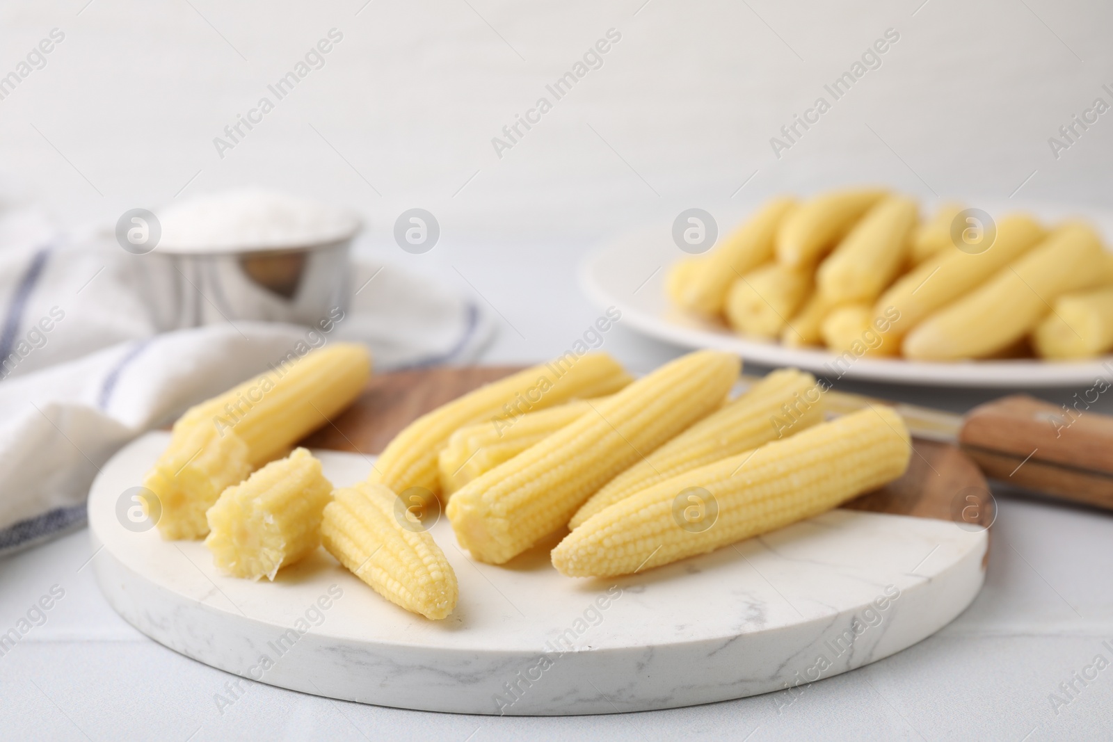 Photo of Tasty fresh yellow baby corns and knife on white tiled table, closeup