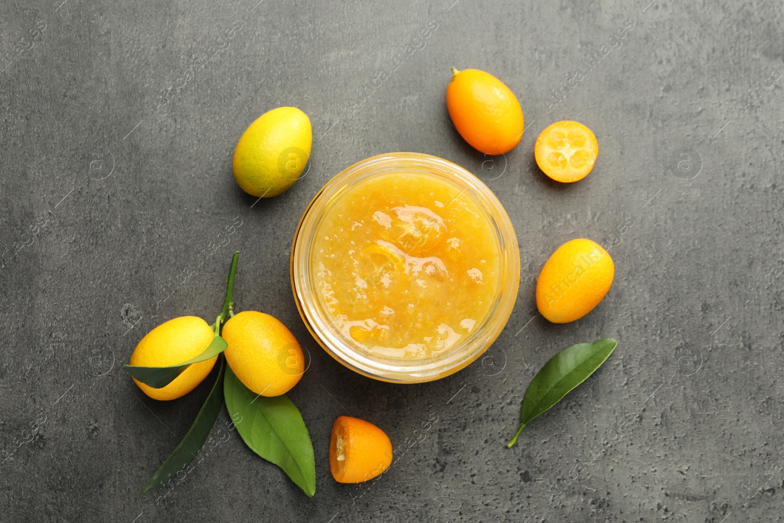 Photo of Delicious kumquat jam and fresh fruits on grey table, flat lay