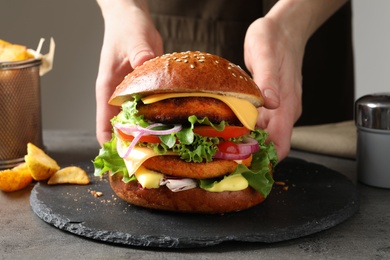 Photo of Woman with double vegetarian burger at table, closeup