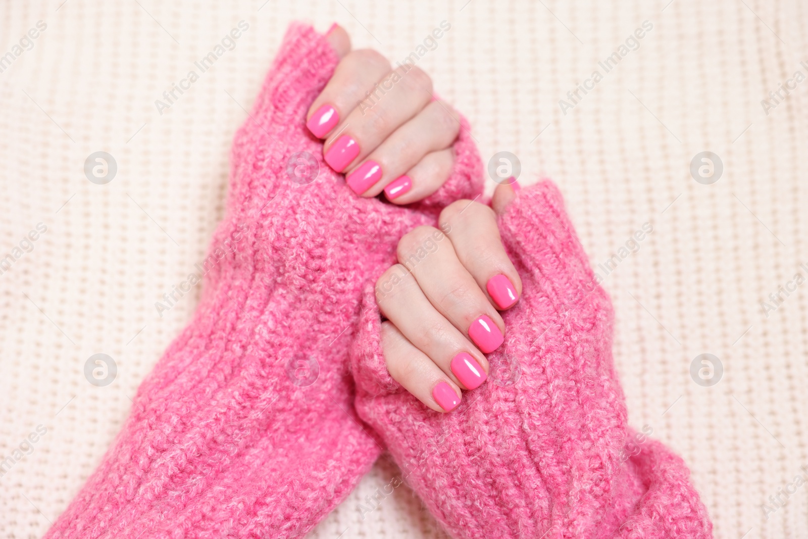 Photo of Woman showing her manicured hands with pink nail polish on knitted blanket, top view