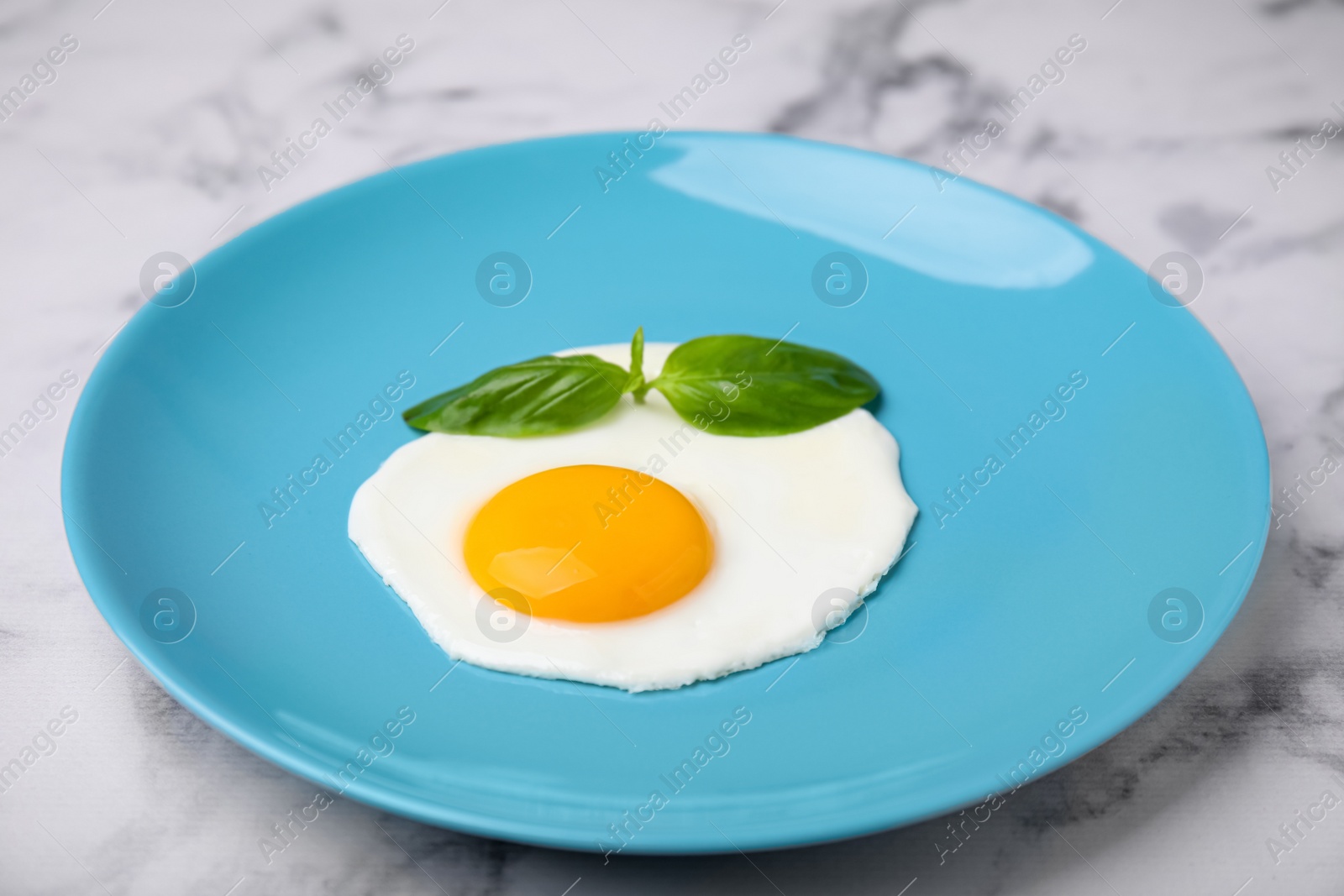 Photo of Tasty fried egg with basil in plate on white marble table, closeup