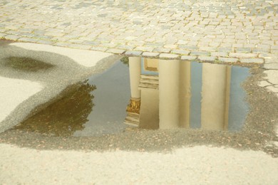 Reflection of beautiful building in puddle on asphalt