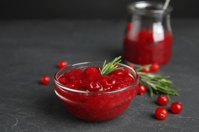 Photo of Bowl of cranberry sauce with rosemary on grey table, closeup