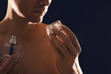 Photo of Young man with perfume bottle on black background, closeup