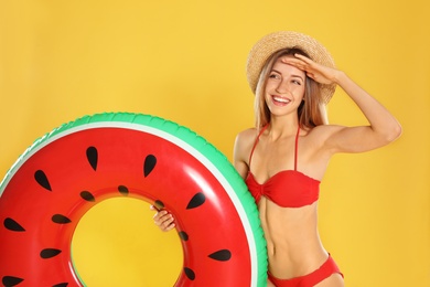 Photo of Beautiful young woman in stylish bikini with watermelon inflatable ring on yellow background