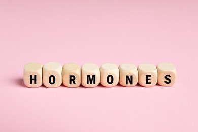 Photo of Word Hormones made of wooden cubes with letters on pink background