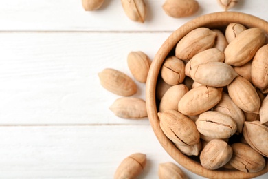 Pecan nuts in bowl on wooden table, top view with space for text