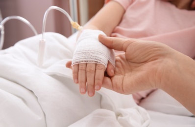 Photo of Doctor holding little child's hand with intravenous drip in hospital, closeup