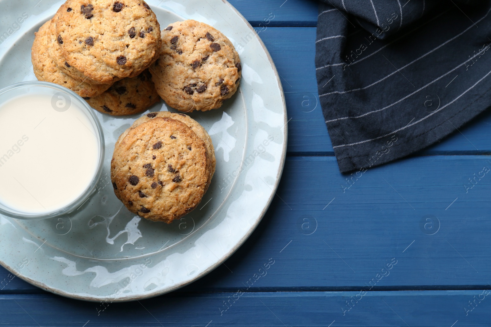 Photo of Tasty chocolate chip cookies and glass of milk on blue wooden table, flat lay. Space for text